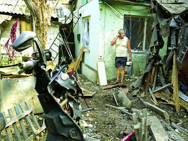کیف: روس کے حامیوں کے حملے کے بعد تباہ شدہ گھر کے پاس شخص موبائل فون پر بات کر رہا ہے