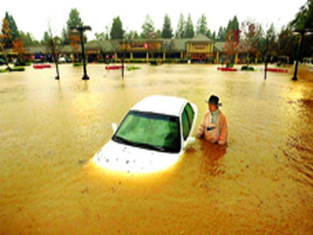 کیلیفورنیا: ایک شخص سیلابی پانی میں گری ہوئی کار کے پاس کھڑا ہے