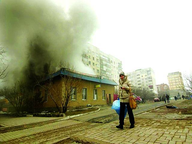 کیف: روسی حامیوں کی جانب سے حملے کے باعث عمارت سے دھواں اٹھ رہا ہے جبکہ ایک رہائشی خاتون پاس سے گزر رہی ہے