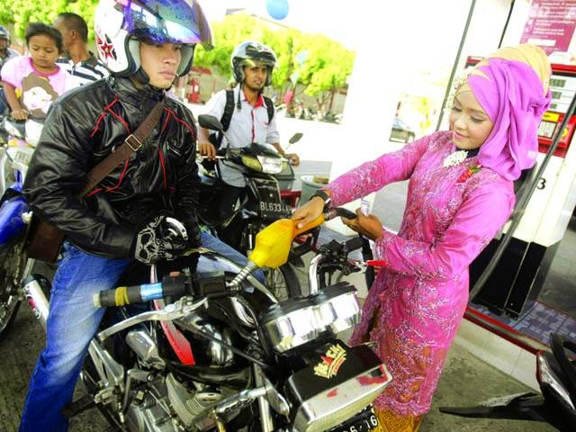 جکارتہ : انڈونیشین خاتون روائتی لباس پہنے موٹر سائیکل میں پٹرول ڈال رہی ہے