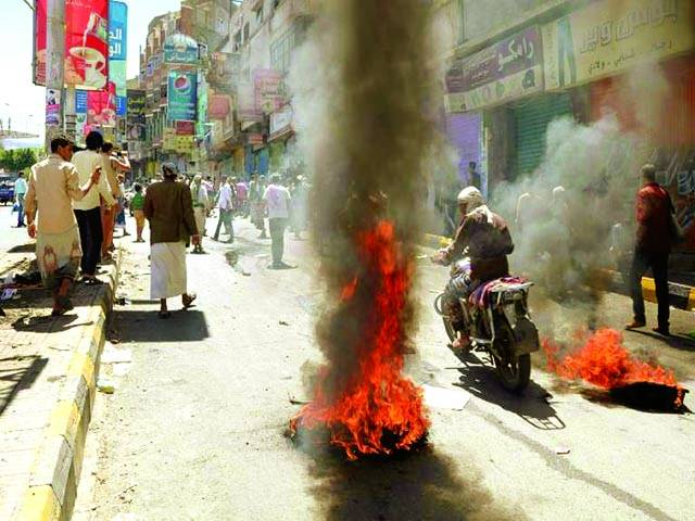  صنعاء: یمن کے شہر تعز میں احتجاج کے موقع پر لوگوں نے سڑک پر ٹائر جلا رکھے ہیں، ایک موٹر سائیکل سوار پاس سے گزر رہا ہے